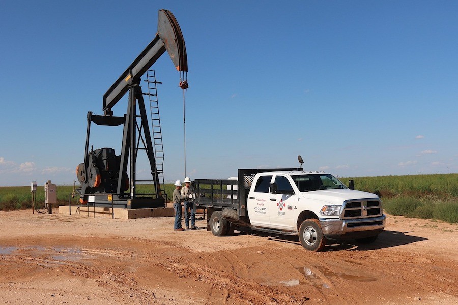 An oil well operating in the background, with workers and a truck in the foreground.