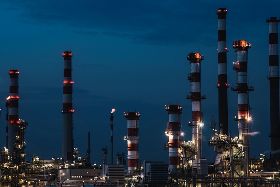 Oil refinery towers lit at night, highlighting energy infrastructure and security needs in the oil and gas industry.