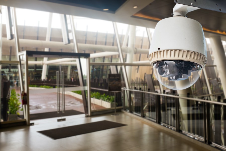 Dome security camera located inside a building entrance with glass doors and windows.