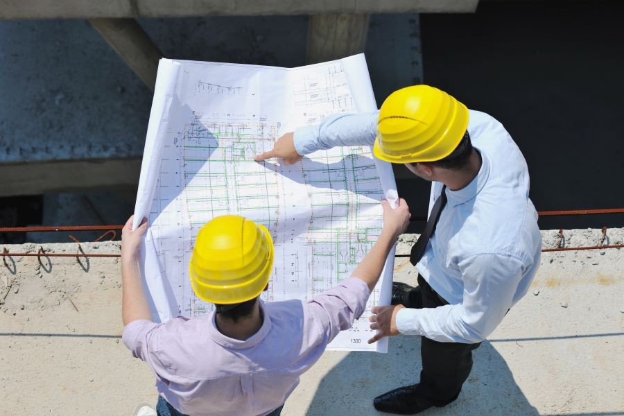 Two men on a construction site looking over the plans.